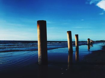 Wooden posts in sea against blue sky