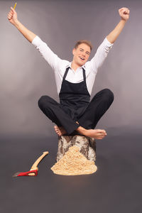 Portrait of young man with arms raised sitting on tree stump