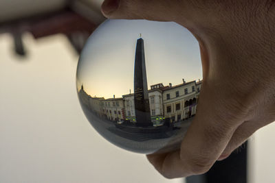 Close-up of hand holding glass building against sky