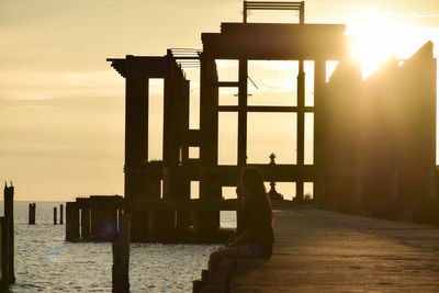 Woman sitting on shore against sky during sunset