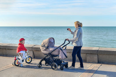 Mother with a stroller and daughter on a bicycle are walking together on the beach
