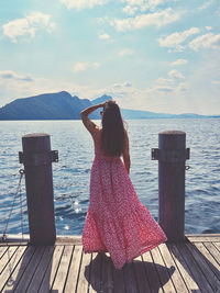 Rear view of woman standing by sea against sky