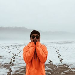 Young man wearing orange hooded jacket standing on snow covered field