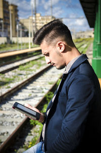 Side view of young man using digital tablet at railroad station