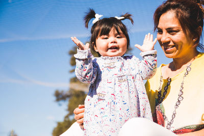 Smiling woman looking at daughter against sky 