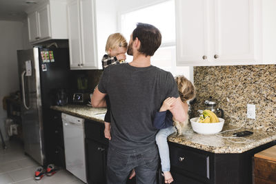 Rear view of father taking care of daughters in kitchen at home