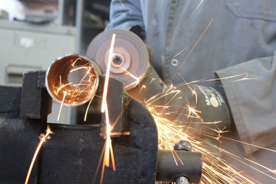 Midsection of worker cutting pipe in factory