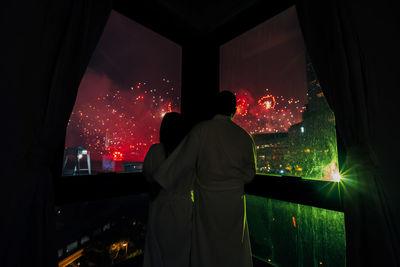 Rear view of man and woman looking firework display through window