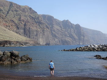 Rear view of man on rock by sea against sky