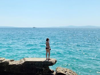 Man standing on rock by sea against clear sky