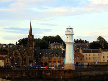 Lighthouse and buildings in city against cloudy sky