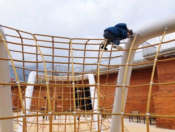 Low angle view of girl playing on outdoor play equipment against cloudy sky