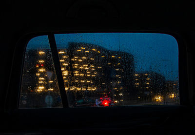 Illuminated cityscape seen through window at night