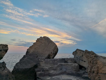 Rocks on sea shore against sky during sunset
