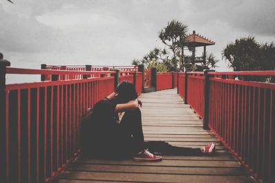 Rear view of woman walking on footbridge against sky