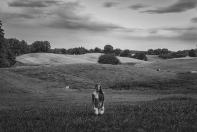 Naked woman kneeling on field against sky