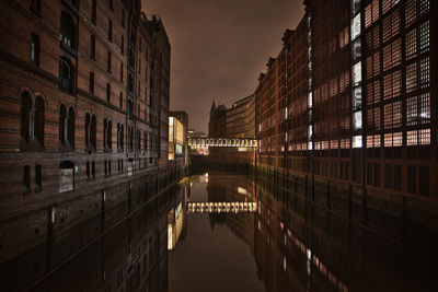 Bridge over canal amidst buildings in city at night