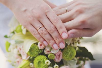 Cropped hands of bride wearing rings touching flowers