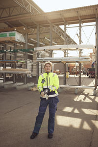 Mature female blue-collar worker in protective workwear standing outside factory