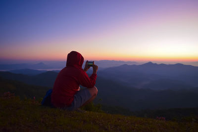 Rear view of man photographing on mountain during sunset