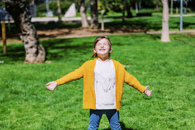 Cute smiling girl with arms outstretched standing on grassy field in park