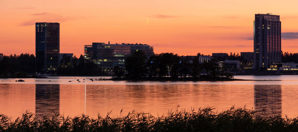 Scenic view of river by silhouette buildings against sky during sunset