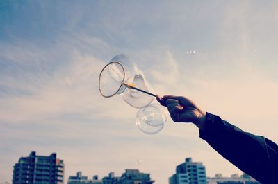 Close-up of hand holding bubble wand against sky