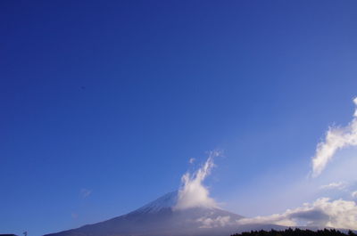 Low angle view of volcanic mountain against blue sky