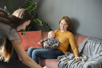 A happy grandmother holding baby grandson on sofa at home living room