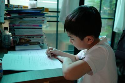 Boy writing on book at table