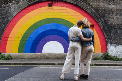 Gay couple standing together in front of rainbow colored wall