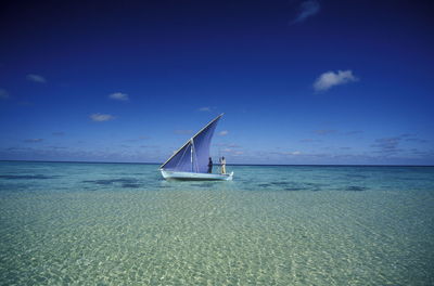 Men sailing boat in sea against blue sky