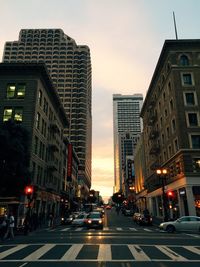 Cars moving on city street amidst buildings during sunset