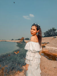 Portrait of smiling young woman standing on land against sky