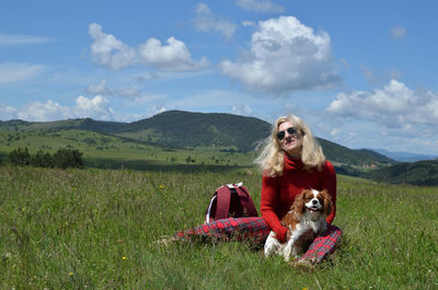 Happy blonde woman in red with her dog cavalier king charles spaniel on a meadow