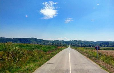 Empty road amidst field against sky