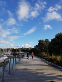 Rear view of people walking on sidewalk in city against sky