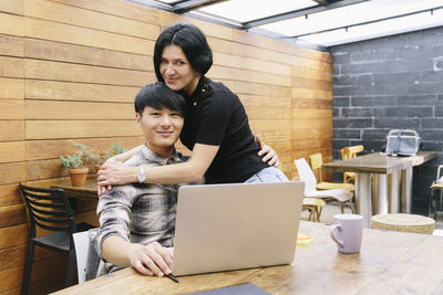 Young woman using phone while sitting on laptop