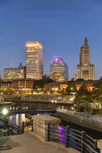 Illuminated bridge over river by buildings against sky at night