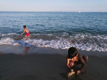 Shirtless boys playing on shore at beach during sunset