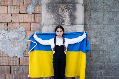 Portrait of girl holding ukrainian flag against wall