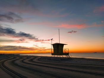 Lifeguard hut on beach against sky during sunset