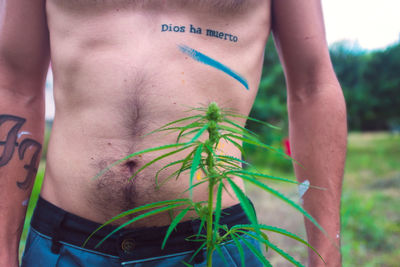 Midsection of shirtless woman standing in plant