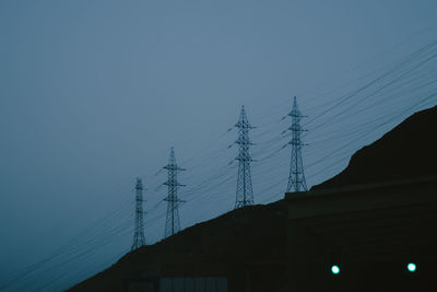 Low angle view of silhouette electricity pylon and building against clear sky