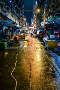 Wet street amidst illuminated buildings in city at night