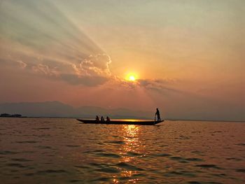 Silhouette people on boat sailing in sea against sky during sunset