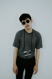 Portrait of young man wearing sunglasses standing against white background