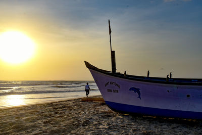 Boat moored on beach against sky during sunset