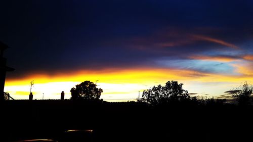 Silhouette trees against dramatic sky during sunset