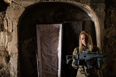 A woman in an army uniform aims to shoot a firearm in an abandoned building. 